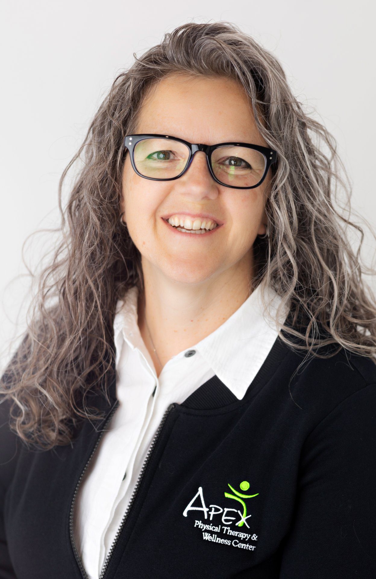 A smiling professional woman named Julia Straley wearing glasses and a black jacket with an embroidered logo for a physical therapy and wellness center.