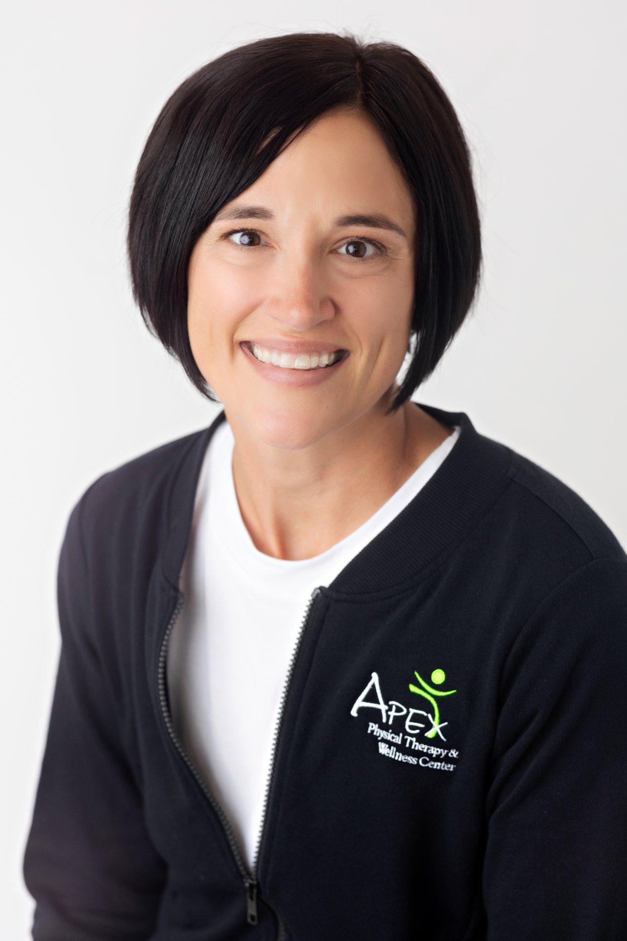 A professional portrait of Kristin Guderian, a smiling woman with short dark hair, wearing a black jacket with the logo 