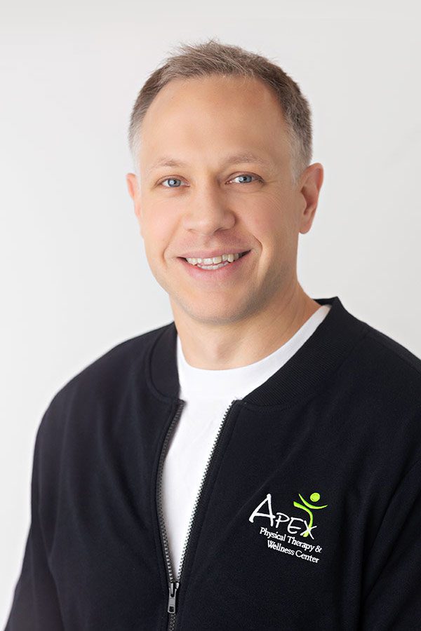 Professional headshot of a smiling man wearing a black zip-up jacket with an 