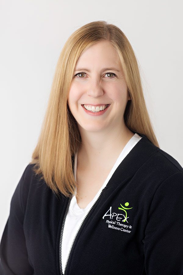 Professional portrait of a smiling woman, Kayla Heger, with long blonde hair, representing her personal brand while wearing a black jacket with an embroidered logo of Apex Physical Therapy & Wellness Center.