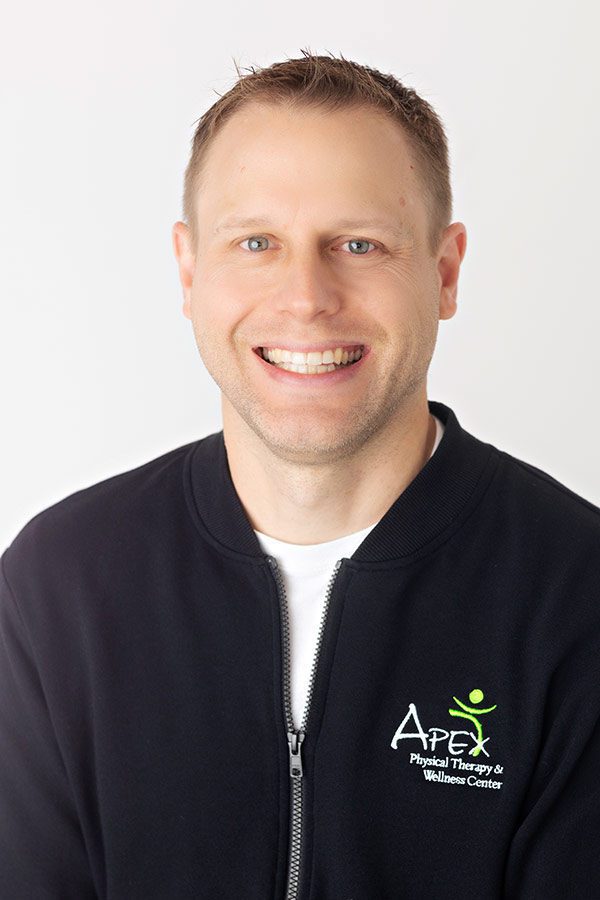 Smiling professional Kameron Ihry Hodem in branded attire ready to assist with physical therapy and wellness services.
