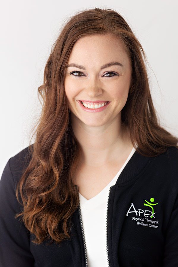 A professional woman named Kayla Heger, with long, wavy hair is wearing a black zip-up jacket with the 