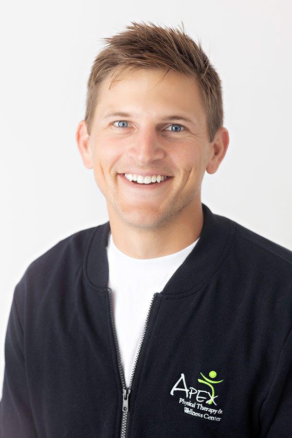 Portrait of a cheerful man with a friendly smile, wearing a black zip-up jacket embroidered with the Rachel Failing health and wellness logo.