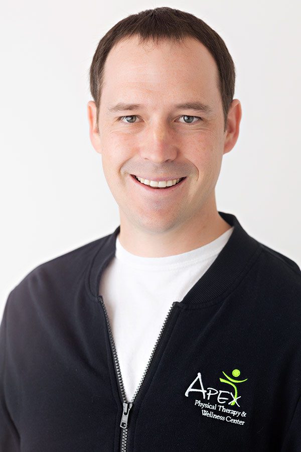 A friendly-looking man with a warm smile, wearing a black zip-up jacket with the logo of 